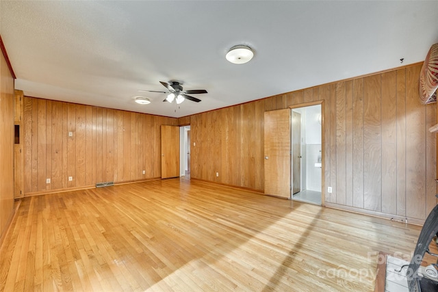 unfurnished room with ceiling fan, wood walls, and light wood-type flooring