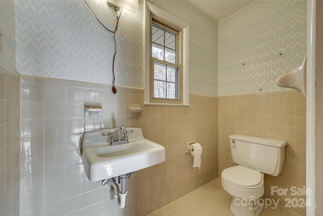 bathroom with toilet, tile patterned floors, tile walls, and sink