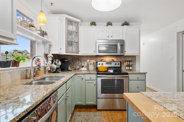 kitchen featuring white cabinetry, sink, hanging light fixtures, stainless steel appliances, and light wood-type flooring