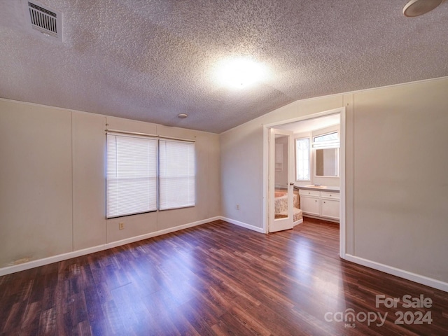 interior space with a textured ceiling, ensuite bath, dark hardwood / wood-style flooring, and vaulted ceiling