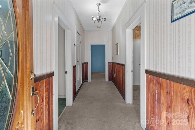 hallway with a chandelier, light colored carpet, crown molding, and wood walls