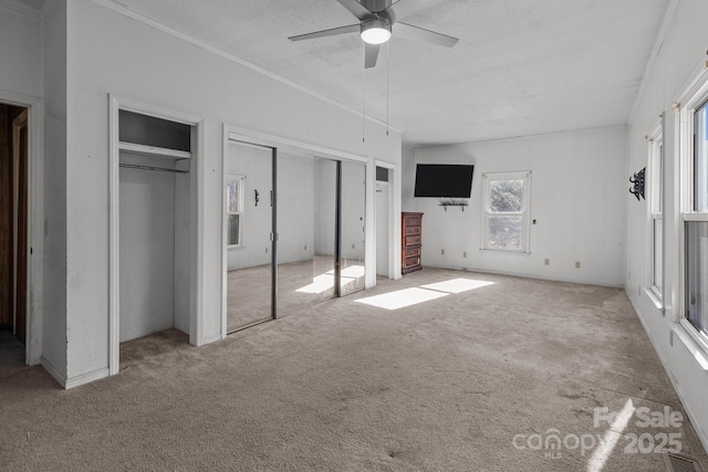 unfurnished bedroom featuring a textured ceiling, ceiling fan, light carpet, and two closets