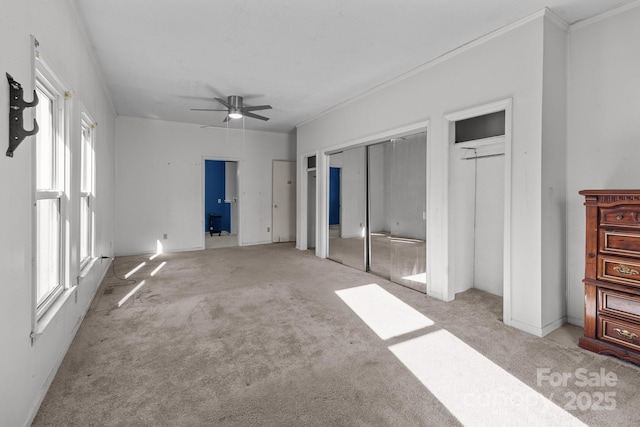 unfurnished bedroom featuring light colored carpet, multiple windows, multiple closets, and ceiling fan