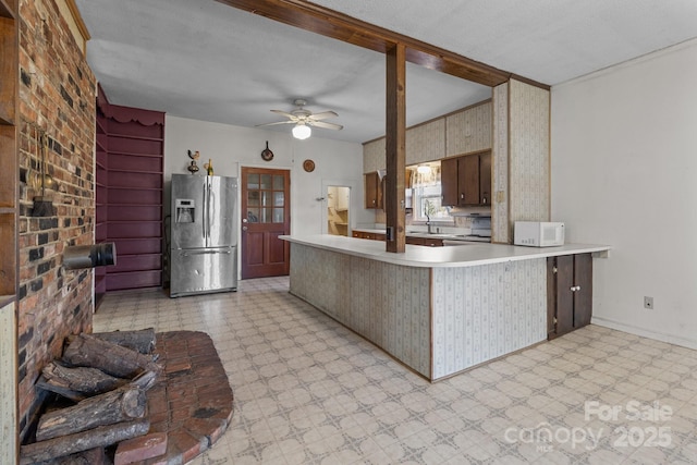 kitchen with kitchen peninsula, stainless steel refrigerator with ice dispenser, brick wall, ceiling fan, and sink