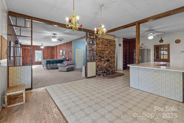 kitchen with beam ceiling, stainless steel refrigerator, wood walls, decorative light fixtures, and light carpet