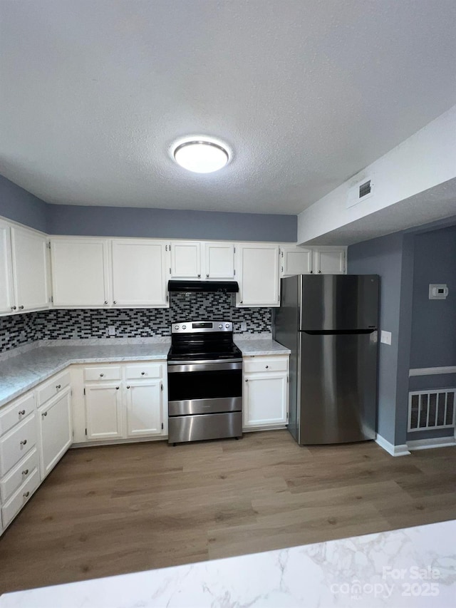 kitchen featuring light wood-type flooring, a textured ceiling, appliances with stainless steel finishes, tasteful backsplash, and white cabinetry