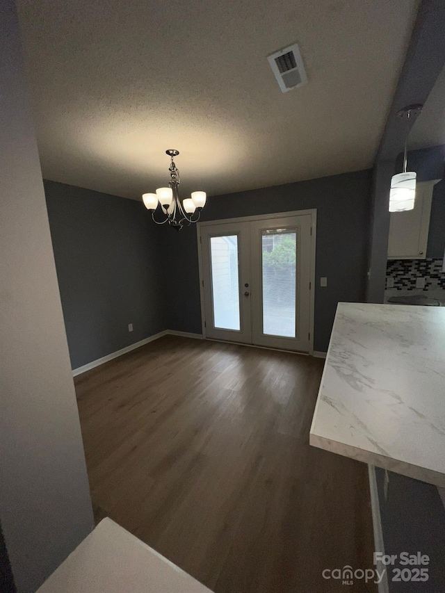 unfurnished dining area with dark hardwood / wood-style flooring, french doors, and an inviting chandelier