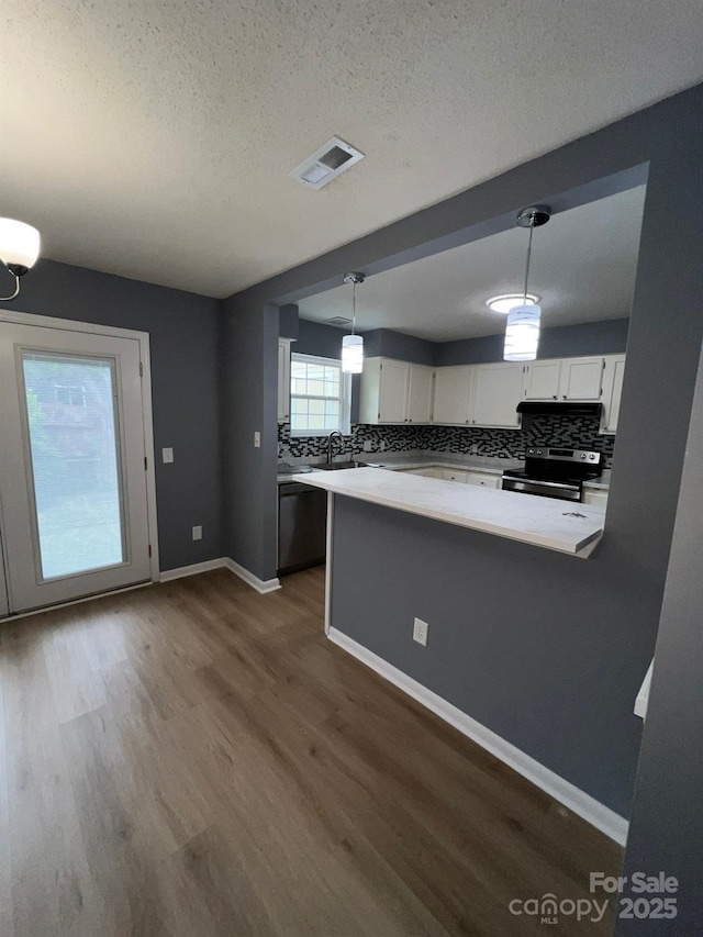 kitchen featuring dark hardwood / wood-style flooring, kitchen peninsula, decorative light fixtures, white cabinets, and appliances with stainless steel finishes