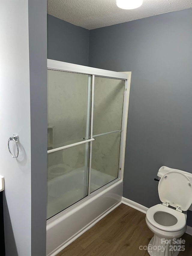 bathroom featuring shower / bath combination with glass door, hardwood / wood-style floors, a textured ceiling, and toilet