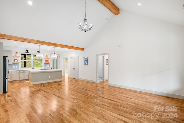 unfurnished living room with beam ceiling, an inviting chandelier, high vaulted ceiling, and light hardwood / wood-style flooring