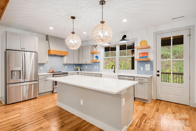 kitchen with light wood-type flooring, stainless steel appliances, a kitchen island, and premium range hood