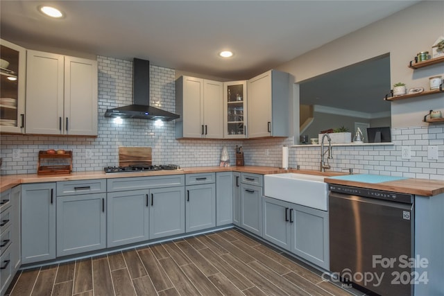 kitchen featuring sink, wall chimney exhaust hood, butcher block countertops, decorative backsplash, and appliances with stainless steel finishes