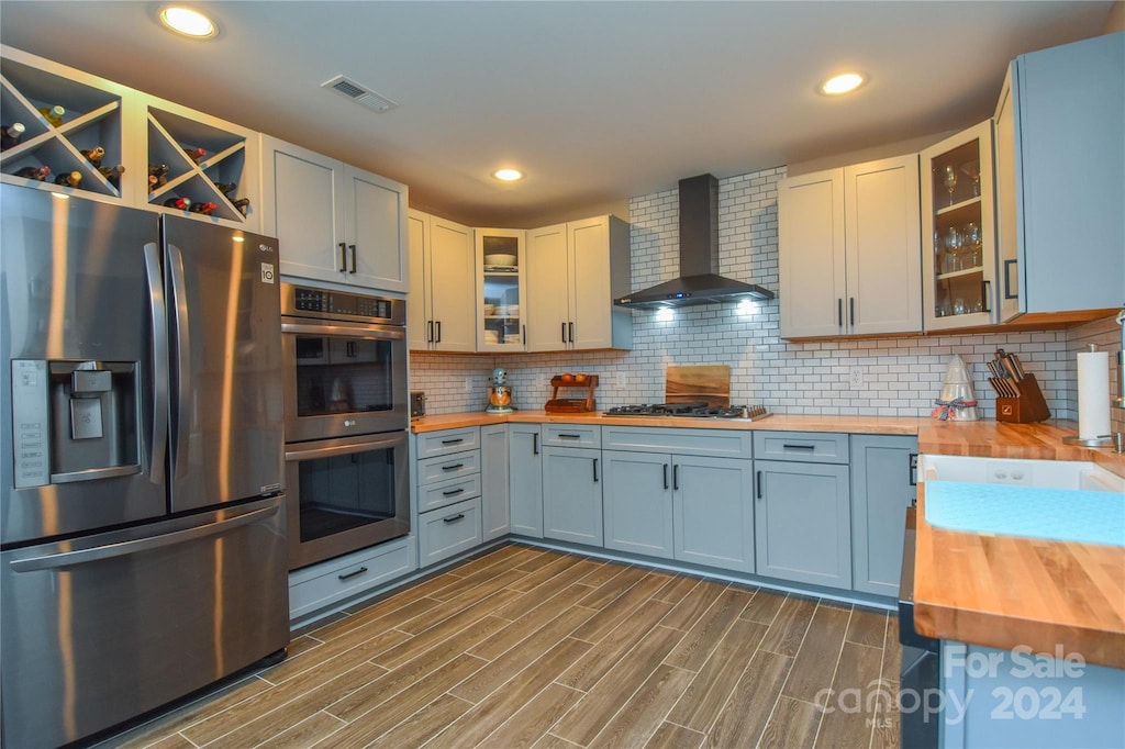 kitchen featuring wooden counters, appliances with stainless steel finishes, backsplash, wall chimney range hood, and dark hardwood / wood-style floors