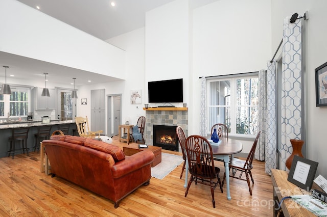 living room with light wood-type flooring, sink, a towering ceiling, and a tiled fireplace