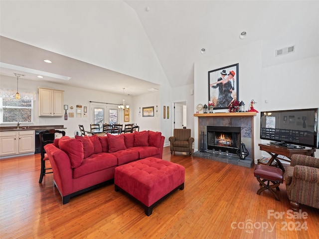 living room featuring light hardwood / wood-style floors, sink, high vaulted ceiling, and a tiled fireplace