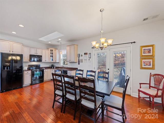 dining space featuring hardwood / wood-style flooring, a notable chandelier, sink, and a skylight