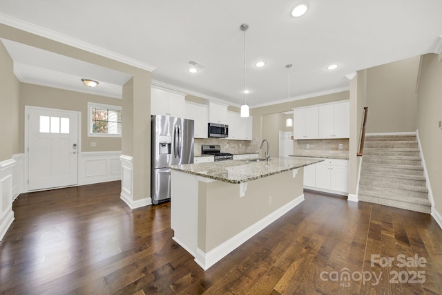 kitchen featuring decorative backsplash, appliances with stainless steel finishes, light stone counters, a center island with sink, and white cabinets