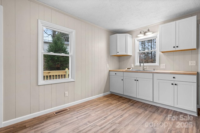 kitchen with sink, white cabinets, a textured ceiling, and light wood-type flooring