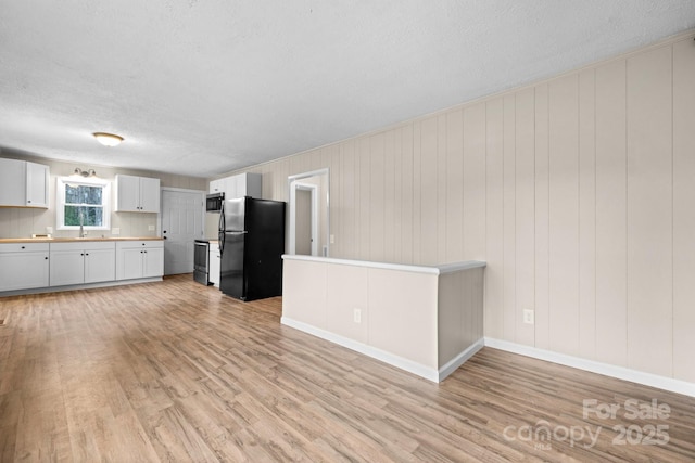 kitchen featuring white cabinets, black fridge, sink, wooden walls, and light wood-type flooring