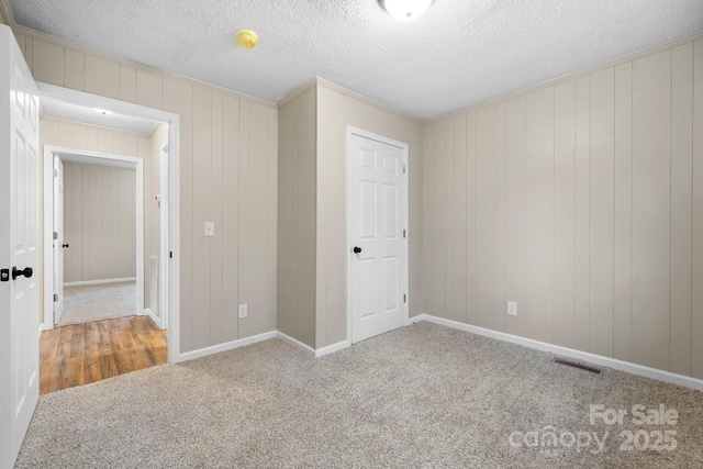 unfurnished bedroom featuring carpet, a textured ceiling, crown molding, and wooden walls