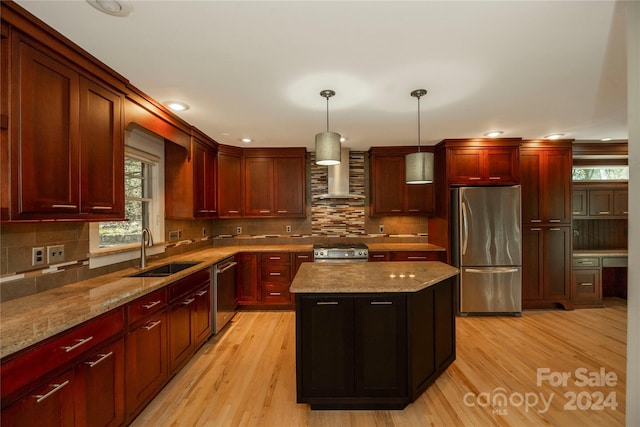 kitchen with sink, hanging light fixtures, wall chimney range hood, a kitchen island, and appliances with stainless steel finishes