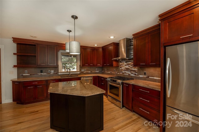 kitchen featuring light stone countertops, a center island, stainless steel appliances, wall chimney range hood, and light hardwood / wood-style flooring