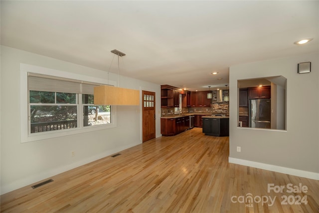 interior space featuring backsplash, stainless steel refrigerator, decorative light fixtures, and light wood-type flooring