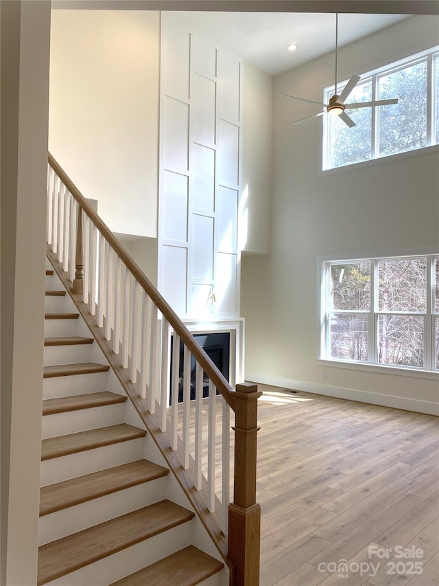 stairway featuring a high ceiling, wood finished floors, a ceiling fan, and a healthy amount of sunlight