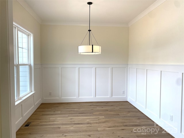 unfurnished dining area featuring crown molding, a decorative wall, visible vents, and light wood-style floors