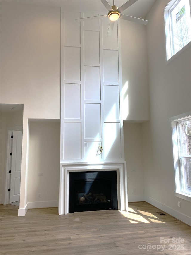 unfurnished living room with a large fireplace, light wood-type flooring, a towering ceiling, and baseboards