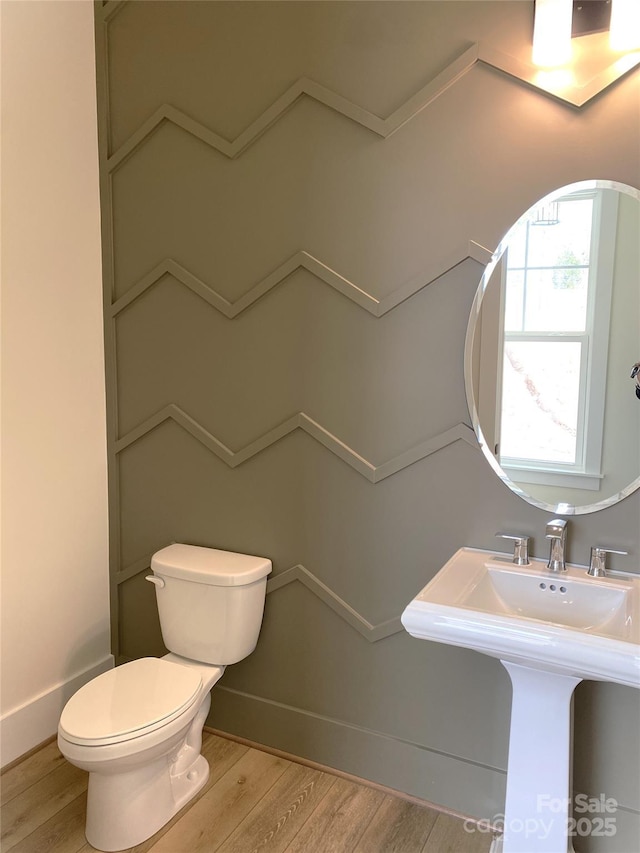 half bathroom with wood finished floors, toilet, and baseboards