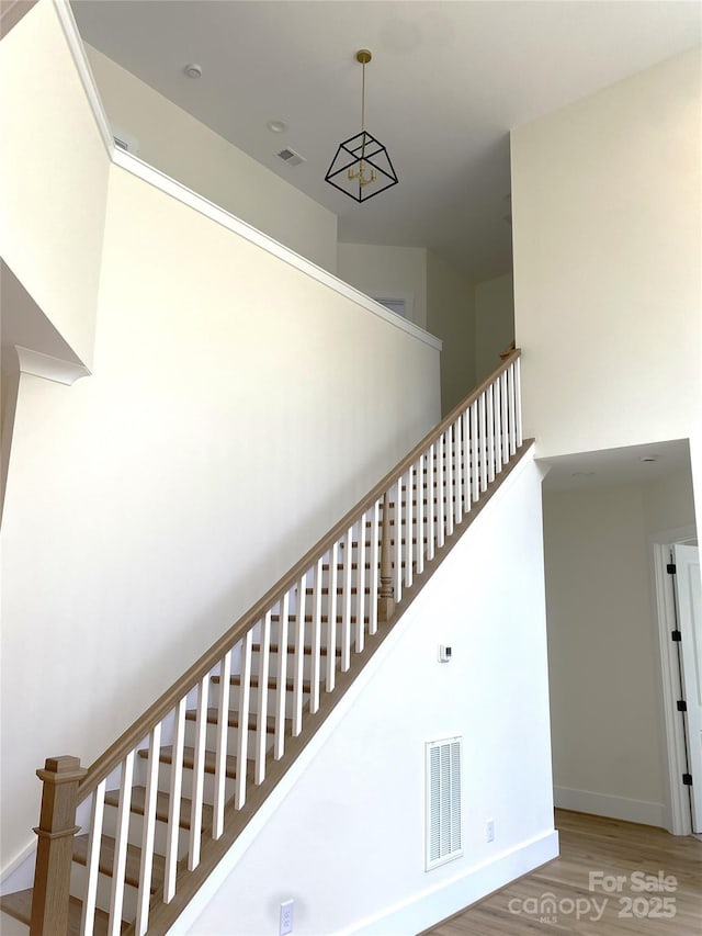 stairs with a high ceiling, visible vents, baseboards, and wood finished floors