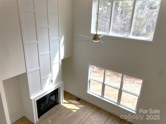 unfurnished living room featuring ceiling fan, light wood-type flooring, a glass covered fireplace, and visible vents