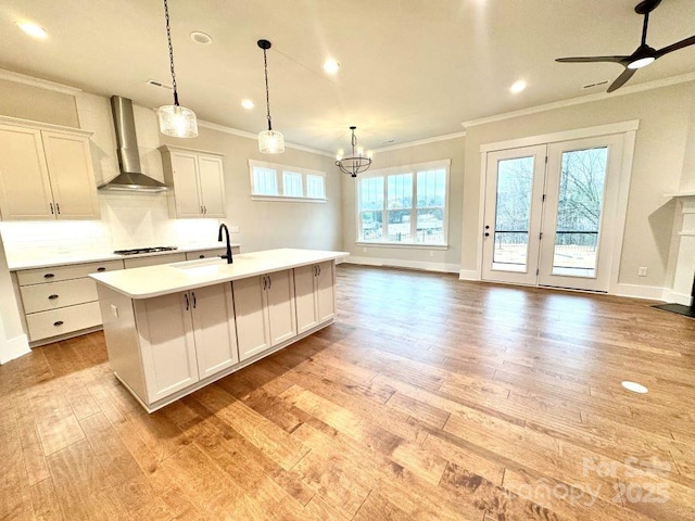 kitchen with a wealth of natural light, sink, wall chimney range hood, pendant lighting, and a center island with sink