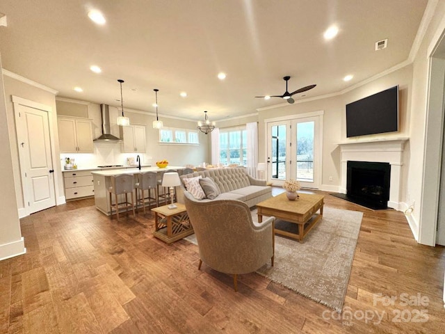 living room featuring ceiling fan, sink, wood-type flooring, and ornamental molding