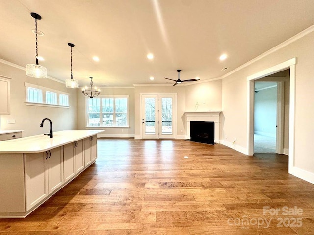 kitchen featuring pendant lighting, a kitchen island with sink, white cabinets, ceiling fan with notable chandelier, and light hardwood / wood-style floors