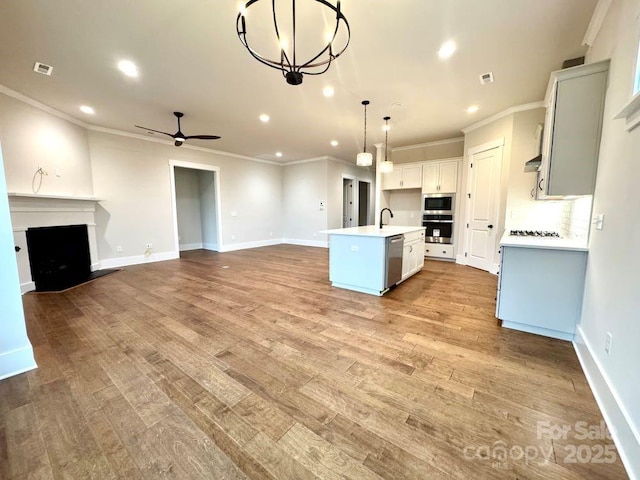 kitchen with pendant lighting, a kitchen island with sink, ceiling fan with notable chandelier, light hardwood / wood-style flooring, and appliances with stainless steel finishes