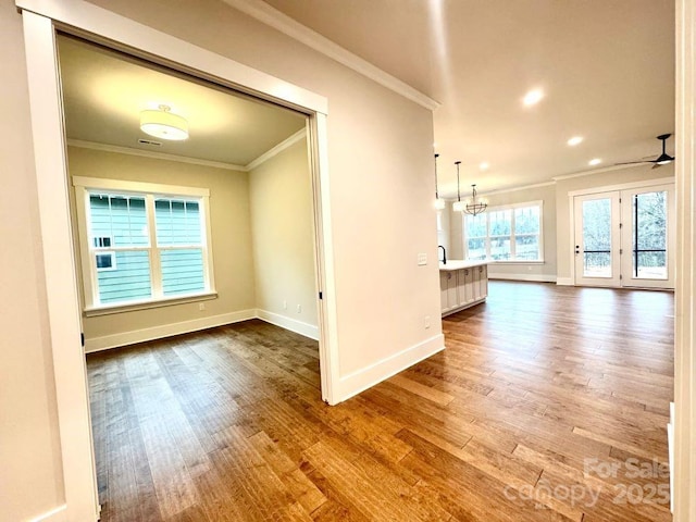 unfurnished living room featuring hardwood / wood-style floors, ceiling fan with notable chandelier, and ornamental molding