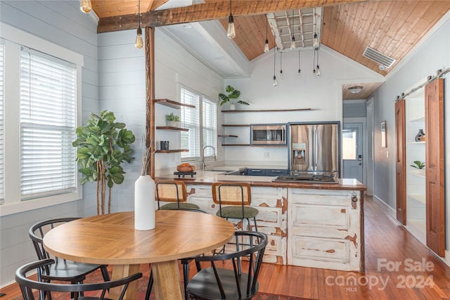 kitchen with lofted ceiling with beams, stainless steel appliances, a barn door, and wooden ceiling