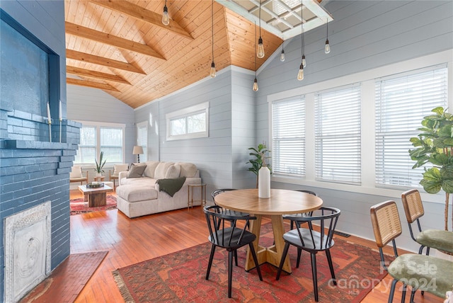 dining area featuring a brick fireplace, wooden walls, wood-type flooring, wooden ceiling, and vaulted ceiling with beams