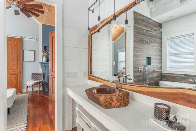 bathroom featuring vanity, lofted ceiling, wooden walls, ceiling fan, and wood-type flooring