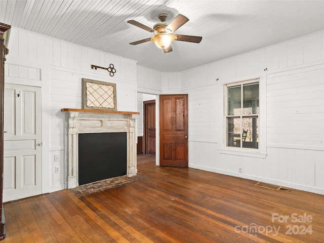 unfurnished living room with ceiling fan, dark wood-type flooring, and wood walls