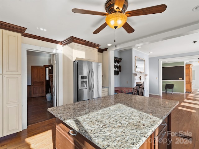 kitchen featuring ceiling fan, stainless steel fridge with ice dispenser, light stone counters, cream cabinetry, and hardwood / wood-style flooring