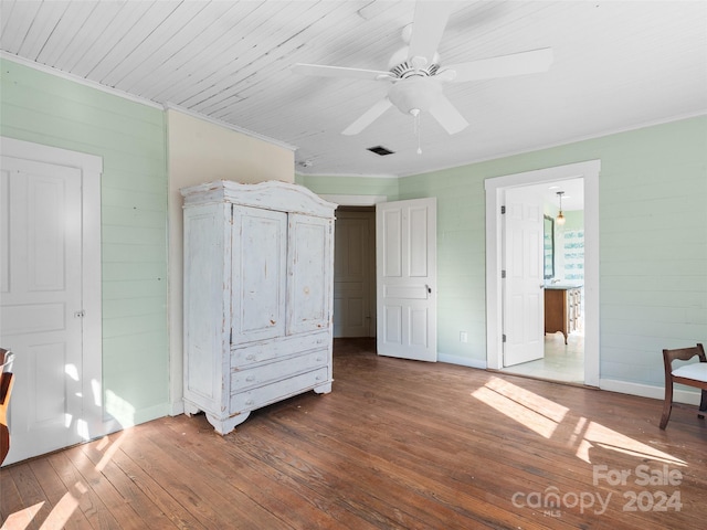 unfurnished bedroom featuring ceiling fan, dark hardwood / wood-style flooring, crown molding, and wooden walls