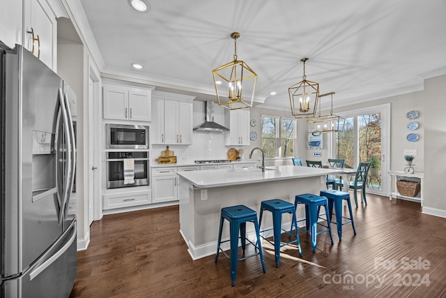 kitchen with pendant lighting, wall chimney exhaust hood, white cabinetry, and stainless steel appliances