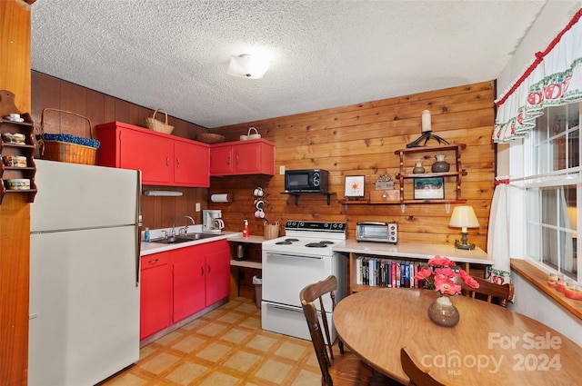 kitchen featuring a textured ceiling, white appliances, wood walls, and sink