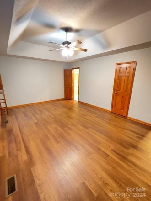 unfurnished room featuring a tray ceiling, ceiling fan, and light hardwood / wood-style floors