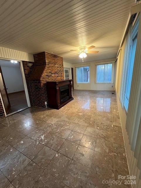 unfurnished living room featuring ceiling fan, a fireplace, and brick wall