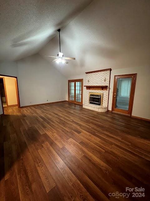 unfurnished living room featuring a brick fireplace, a textured ceiling, vaulted ceiling, ceiling fan, and dark wood-type flooring