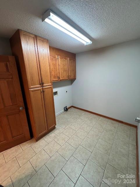 laundry area with electric dryer hookup, cabinets, and a textured ceiling